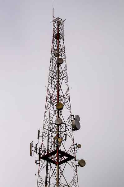 tall metal tower with various satellite dishes cell phone receivers and transmitters and wires