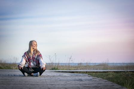 A portrait of Randi, the breathwork facilitator smiling rested in nature with blue skies loving the ability to educate humans on their breathwork and nervous system supports to help the population.