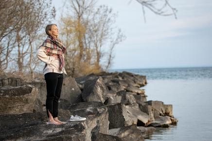 An woman rejuvenating herself standing on the rocks by a serene lake allowing functional breathwork to support her nervous system.