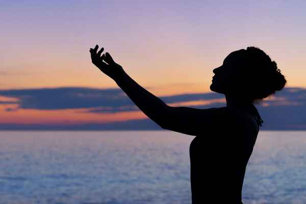 Woman with hands raised up infront of ocean at sunset