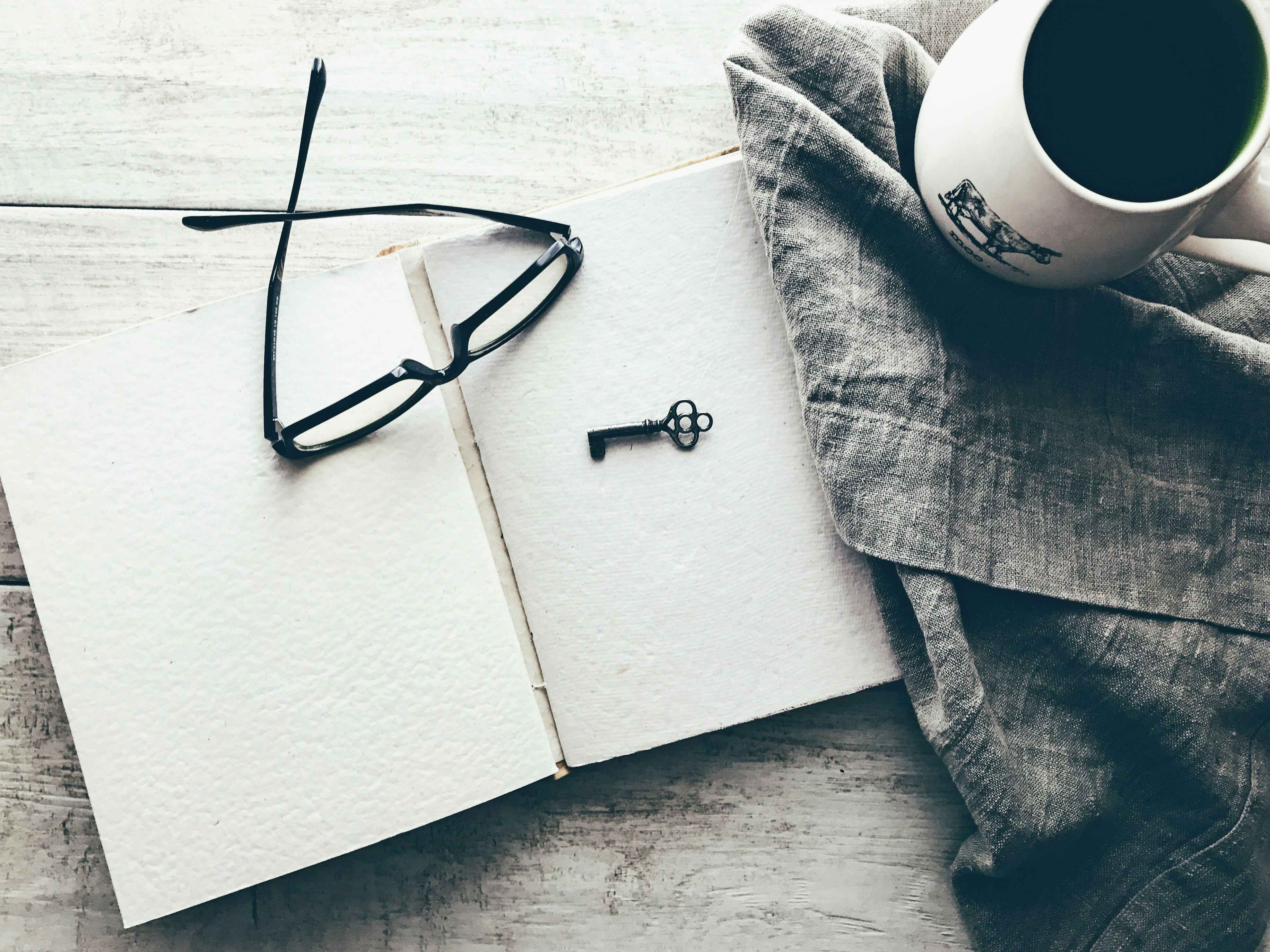 A journal and pen rest on a table with a cup of coffee next to them. 