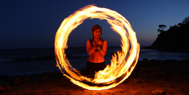 A woman fire dancer at a beach spinning a ring of fire
