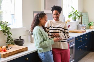 Black mother and daughter in kitchen smiling and talking to each other.