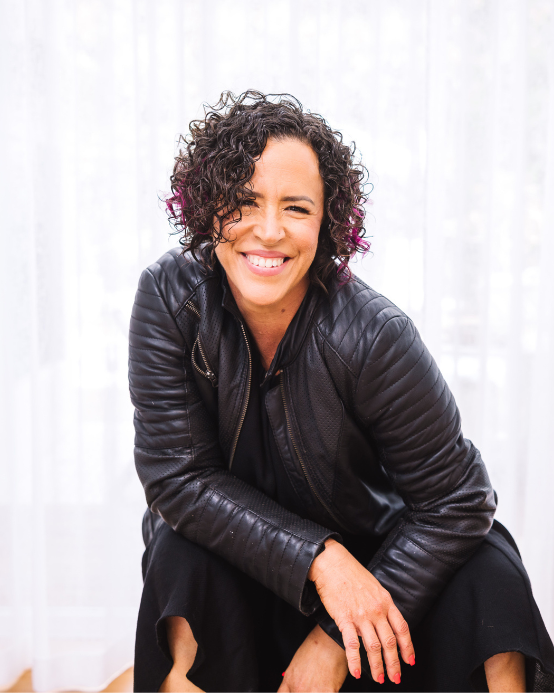 Magnetic Messaging Mentor Kylie - a woman with dark curly hair wearing a black leather jacket and smiling at the camera