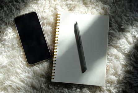 A blank journal page with a pen sits on a fluffy white rug. A cell phone is next to the journal.