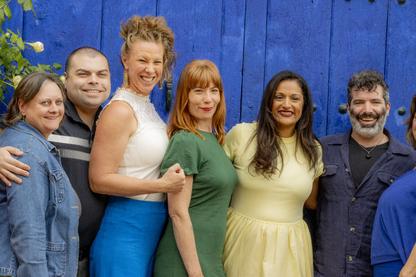 A joyful group of Awaken retreat participants standing together in front of a bright blue door in Spain, embodying empowerment coaching through community, belonging, and shared growth.