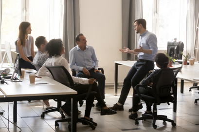 An executive leadership coach speaking to his business team who are gathered around him for leadership development
