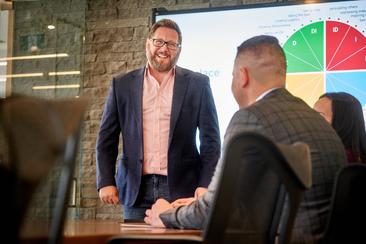 Ryan Quesnel smiling big while presenting executive leadership coaching session standing in front of a business team in a board room