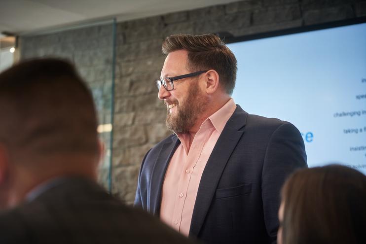 Ryan Quesnel smiling big while presenting DiSC leadership development workshop results as he stands in front of a team of executives in a board room