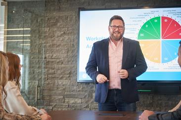 Ryan Quesnel smiling big while presenting executive leadership coaching session standing in front of a business team in a board room