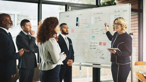 An executive leadership coach standing and writing on a whiteboard while talking to her team