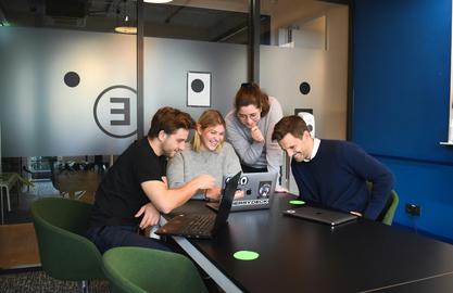 business team gathered around a laptop, smiling and talking to eachother