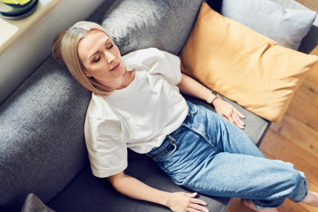 Kvinde ligger med lukkede øjne i sofaen og slapper af