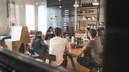 Team gathered around a boardroom table having a discussion about the five behaviours of a cohesive team workshop 