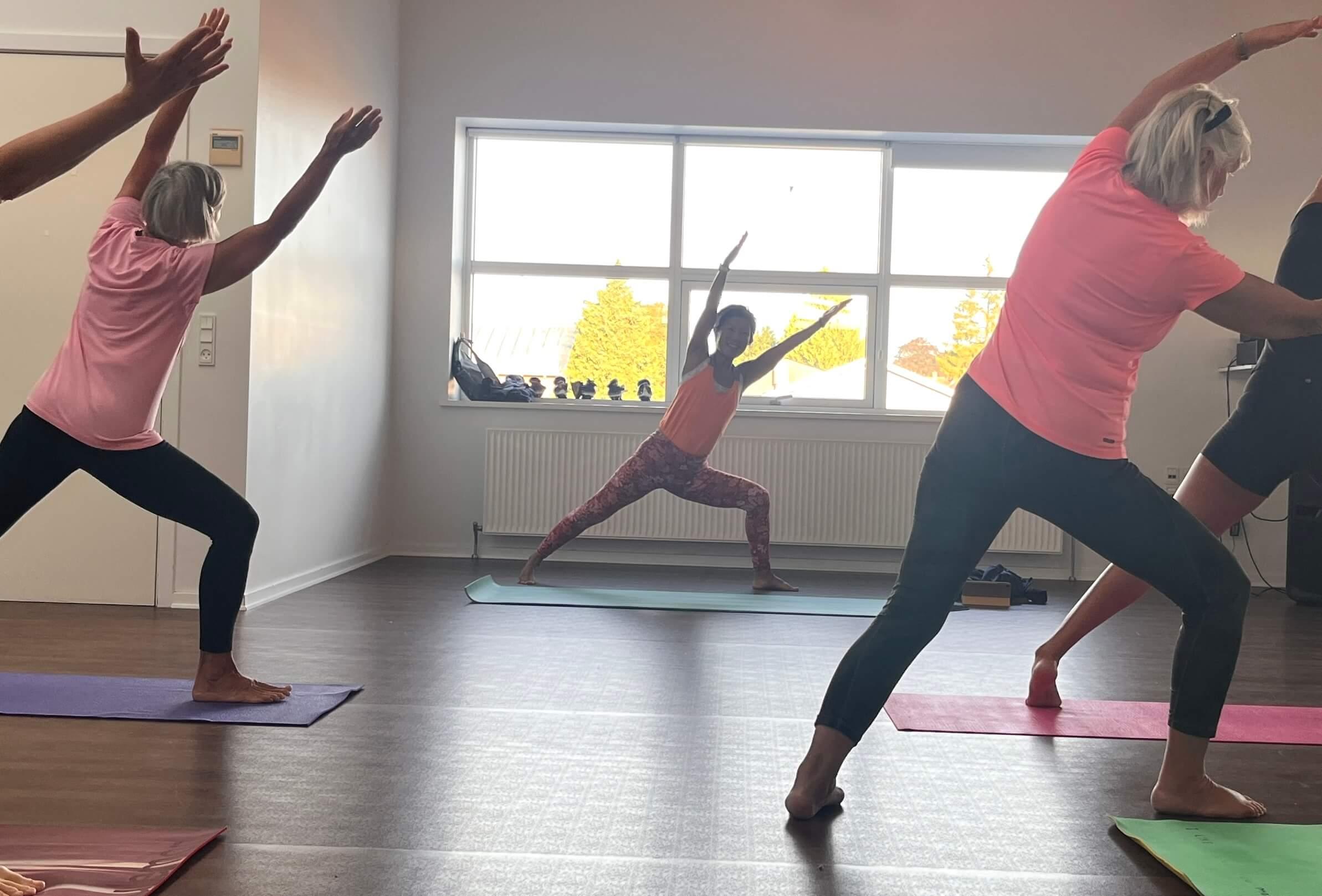 Et yoga hold hvor instruktøren står foran et vindue