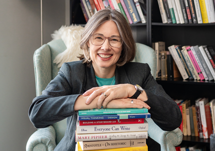 Dawn next to her book shelf with pile of books in front of her