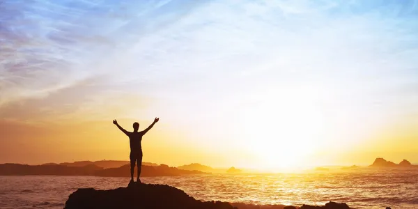man on rock by ocean at sunset