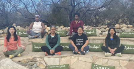 Six women practice the REST meditation technique outside during a retreat for women in healthcare, with green pillows and several layers of stone seating