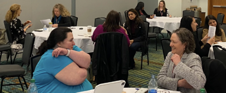 Two women seated at a table in a conference room practice tapping at a tapping workshop