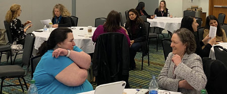 Two women sitting at a table in a conference room practicing tapping and smiling.