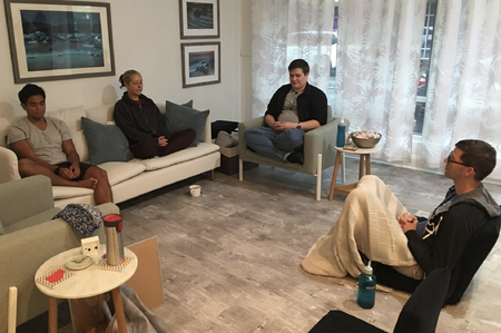 Four people sitting comfortably meditating on the floor and on furniture.