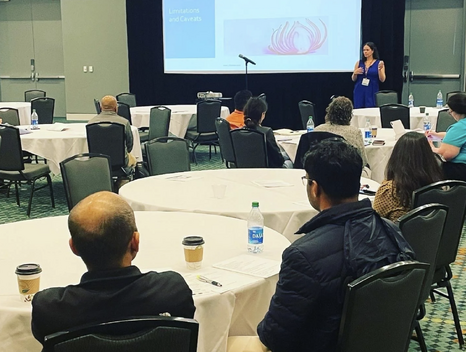 Jill delivers a tapping workshop in a conference room with multiple people seated in chairs facing her