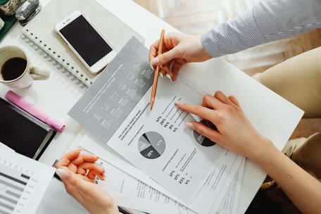 Top-down view of hands pointing to printed infographics and pie charts on a desk next to a smartphone and a coffee cup.