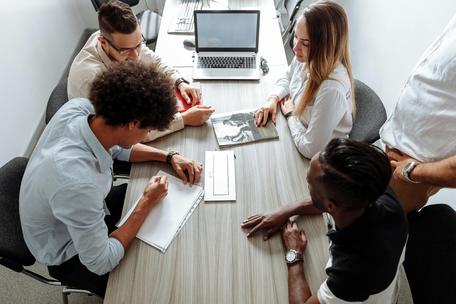 High-angle view of a diverse team collaborating around a long conference table with a laptop, notebooks, and documents.