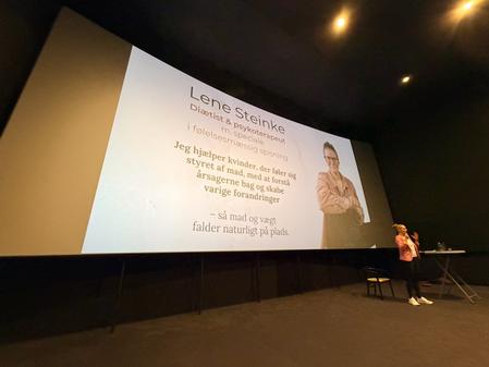 Lene Steinke, diætist og psykoterapeut står foran lærred i biograf og holder foredrag om mad og følelser i et omsorgsfag