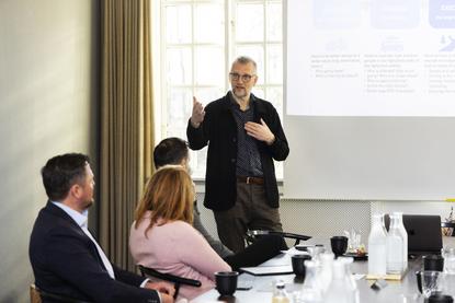 A male speaker presents a digital transformation and implementation framework to corporate leaders in a meeting room, illustrating leadership training for organizational AI adoption.