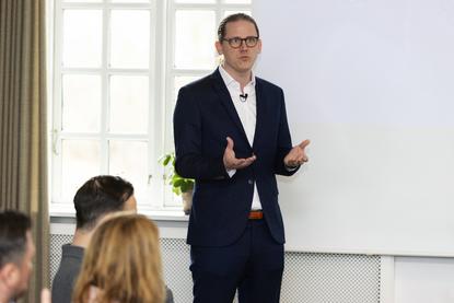 A corporate trainer stands before a boardroom table presenting on a projector screen, leading an AI training workshop on organizational transformation for a group of professionals.