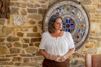Christi Byerly, MCC stands in front of stained glass artwork holding a scallop shell, symbol of Spain's ancient pilgrimmage on the camino de santiago