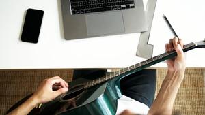A person looking at a laptop playing a guitar