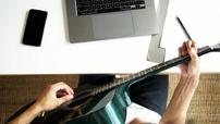 A person looking at a laptop playing a guitar