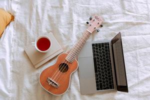 A cup of tea, a ukulele, and a laptop on a white sheet