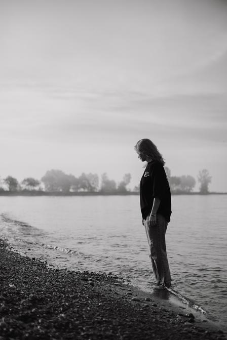 A woman walking along the water's edge while in deep thought about her symptoms of anxiety and ease of irritability when nothing has come to aid her nervous system safety.