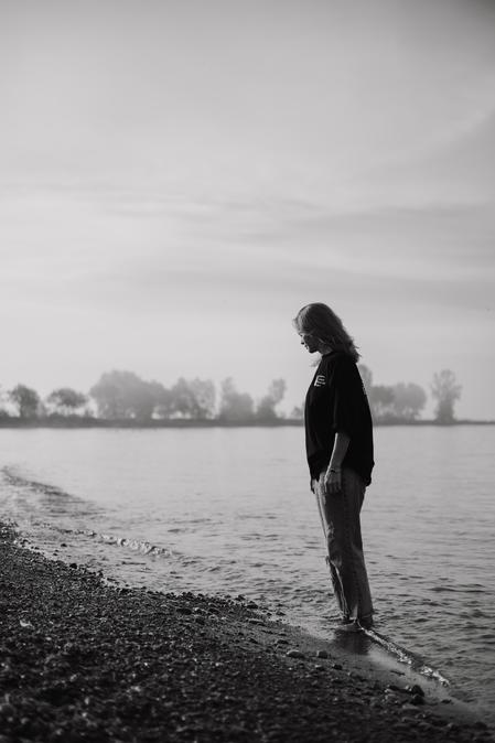 A woman walking along the water's edge while in deep thought about her symptoms of anxiety and ease of irritability when nothing has come to aid her nervous system safety.