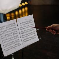 A hand pointing to a piece of sheet music with a pencil