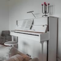 A white upright piano in a white room with white and grey furniture