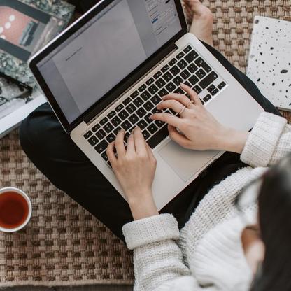 A woman in a white sweater typing on a MacBook