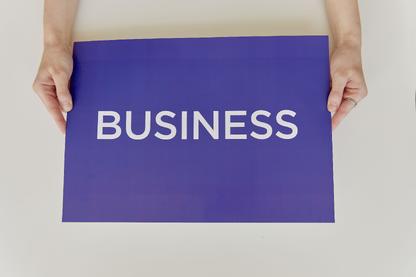 Hands holding a blue sign with "Business" written in white letters