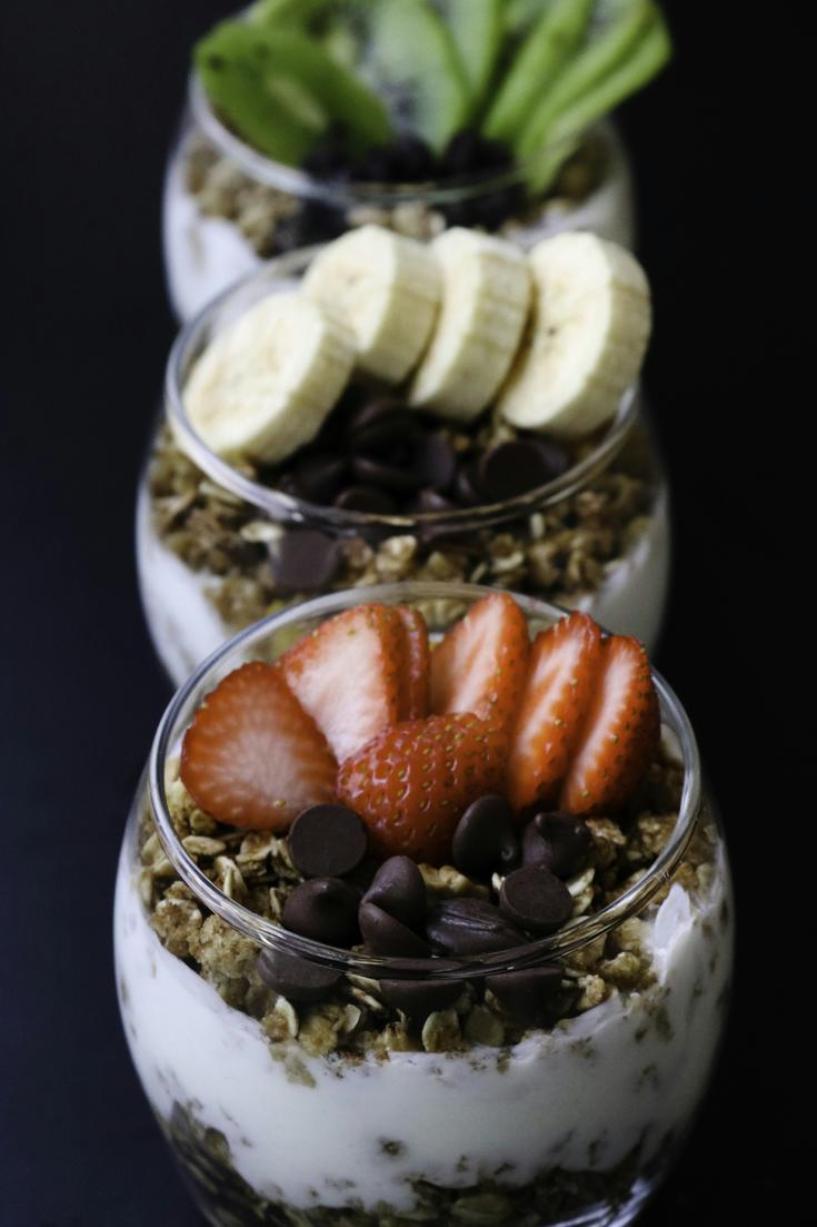 Three small Greek yogurt parfaits topped with strawberries, banana, granola, and chocolate chips