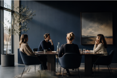 Four colleagues in quiet conversation around a table in a calm, daylit meeting room