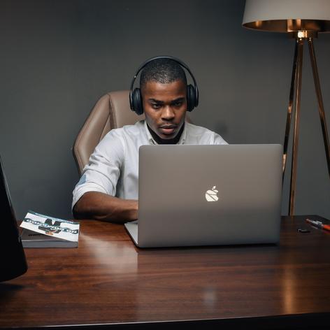 Black man wearing headphones typing on MacBook