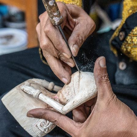 Hands using a pointy tool to carve a wooden sculpture
