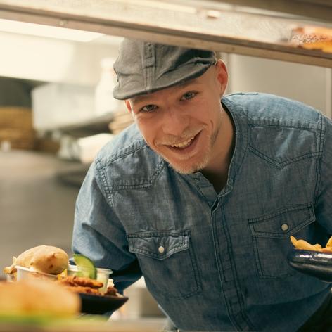 A man in a denim shirt smiling as he serves food