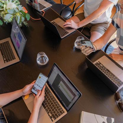Four people working on laptops with phones at a long table