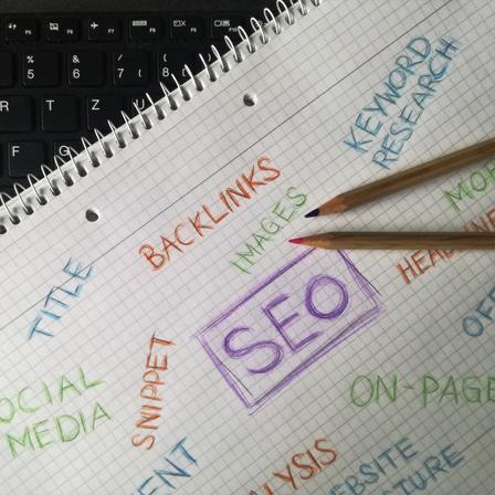 The letters "SEO" in a purple box handwritten on graph paper surrounded by other SEo terms