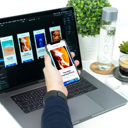 A hand holding a cell phone in front of a laptop with the phone screen showing one of the website templates on the laptop screen