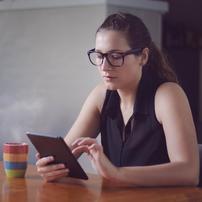 A woman typing on a tablet at a table with a coffee mug